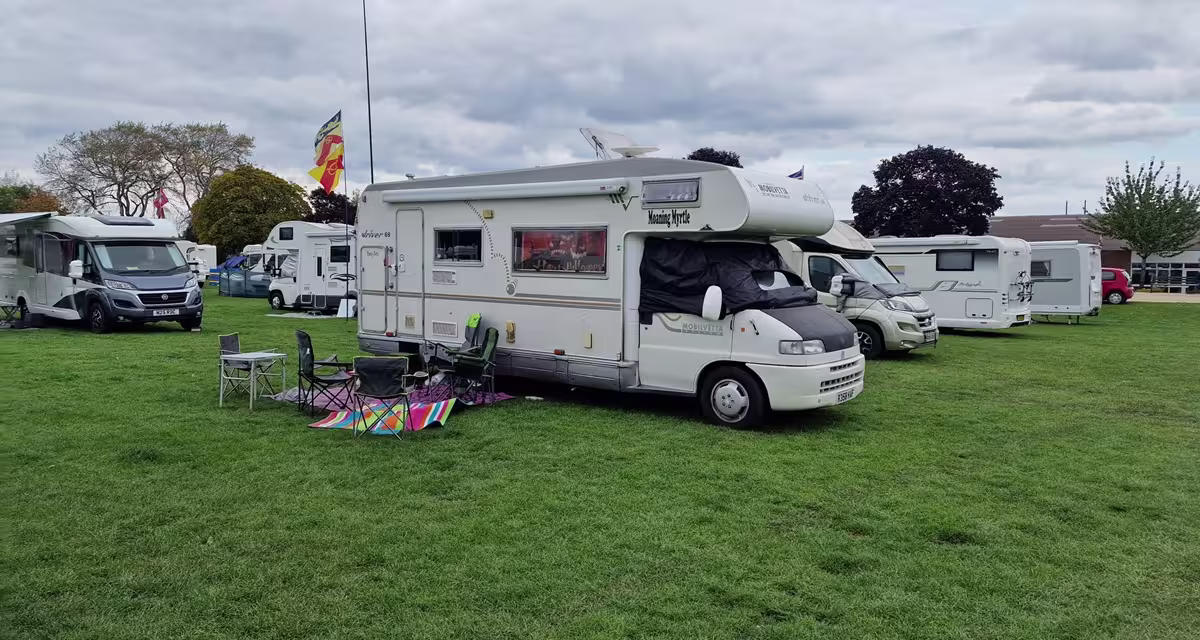 A family motorhome parked at an official campsite surrounded by tall pine trees